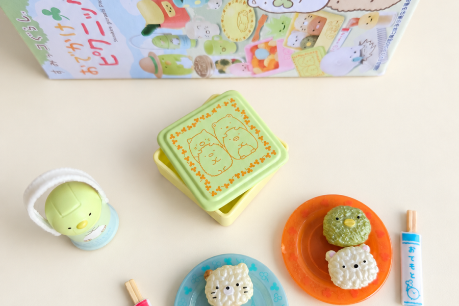 Sumikkogurashi miniature rice-ball characters on blue and orange plates, a tiny lunchbox, bottle and chopsticks with their packaging.